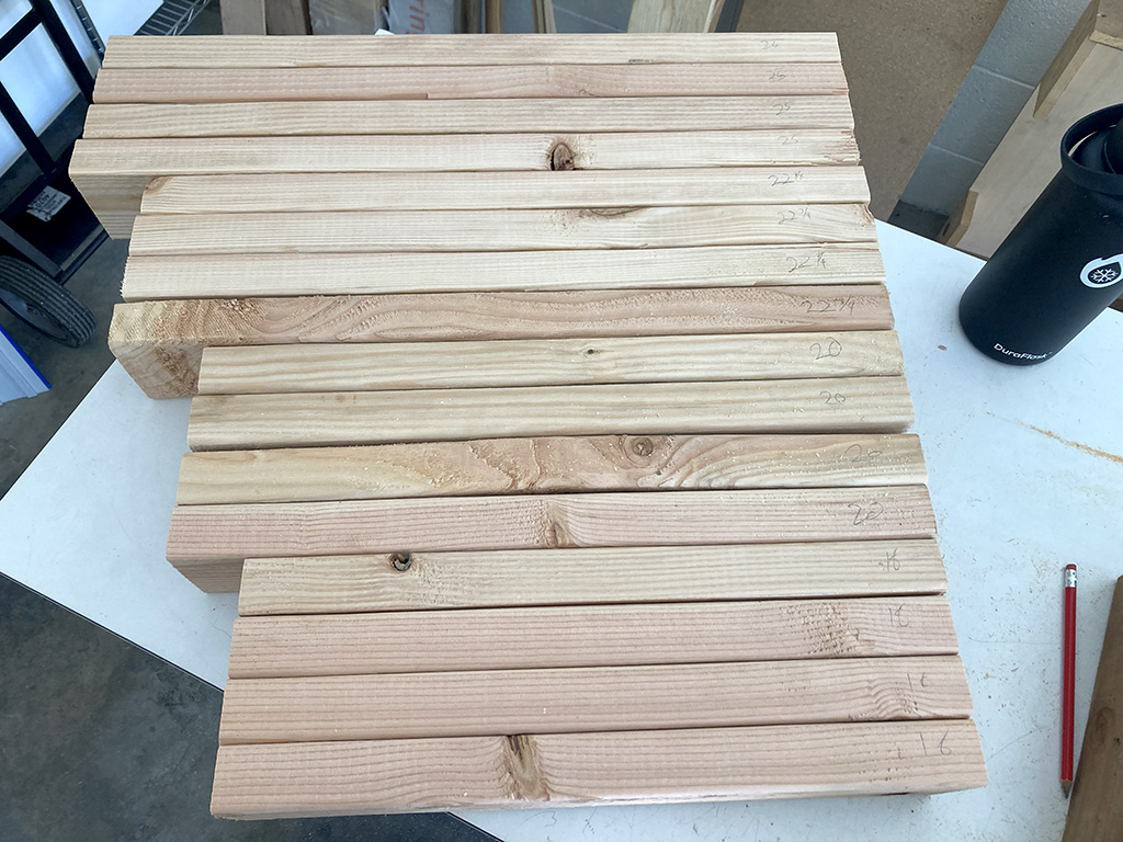 Photo of finished 2x4 cuts organized in groups of 4 lengths, each with 4 lengths for a total of 16 pieces; the lengths of each piece are lightly penciled on the edges
