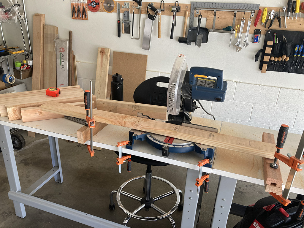 Photo of workbench centered on miter saw with 2x4 prepared to be cut; some finished 2x4 cuts lie to the left of the saw