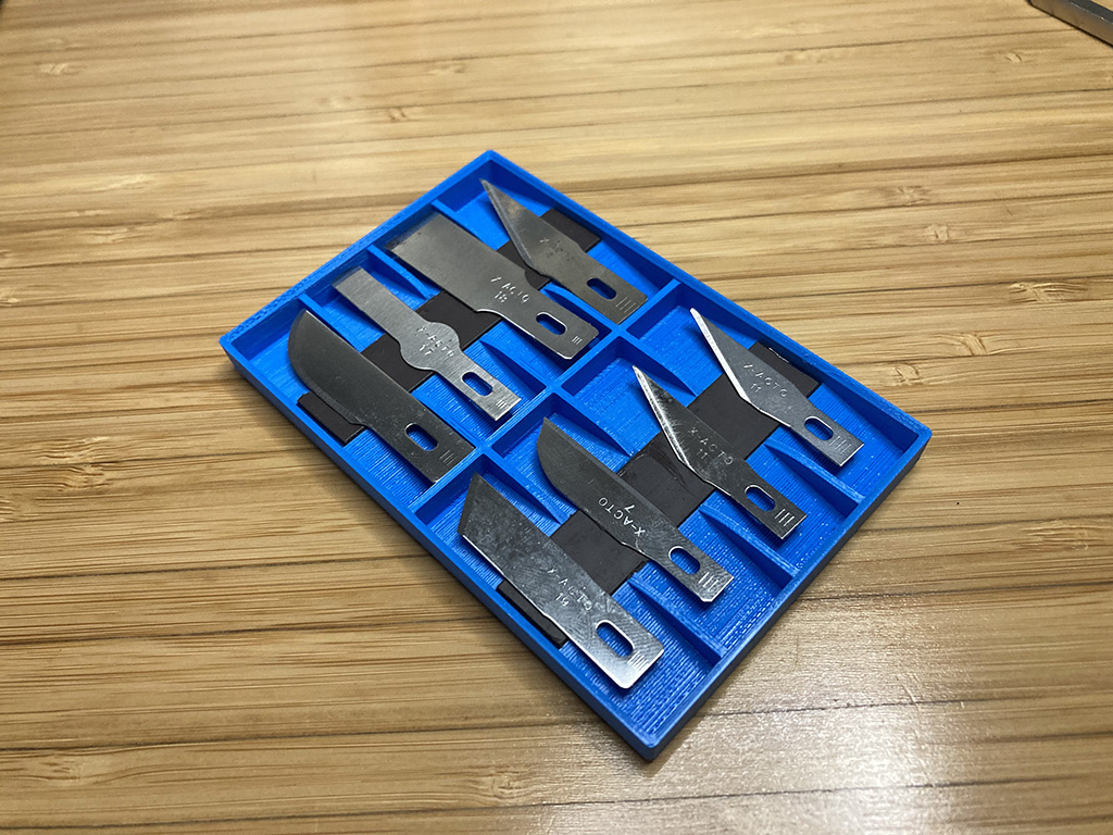 Photo of finished blade holder showing two rows of four blades on a relatively thin plastic card. There are compartments for each blade and the blades are held in place by a magnetic strip across each of the two rows.