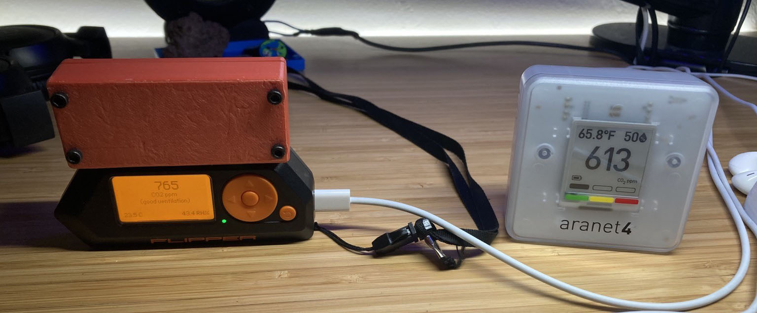 Photo of my DIY CO2 sensor running of a Flipper Zero reading 765ppm and an Aranet4 sensor reading 613ppm